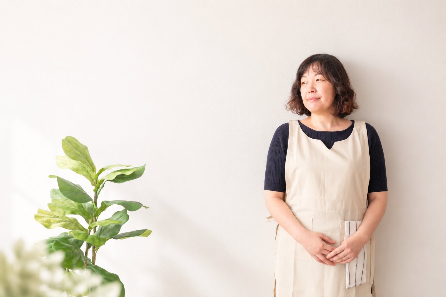窓辺の自然光の中で、家事の手を止めて立つcocoriaの提供者